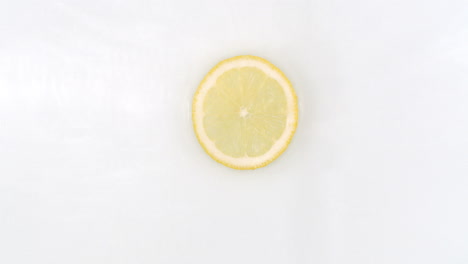 Wasserspritzer-In-Zeitlupe-Auf-Einer-Zitronenscheibe,-Die-Auf-Weißem-Hintergrund-Im-Wasser-Liegt